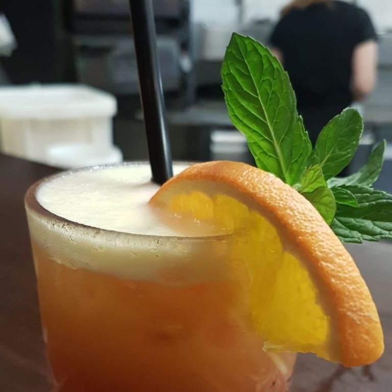 Cocktail mit orangefarbener Garnitur und Minzblatt auf einem Tisch.