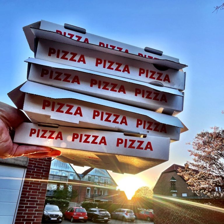 Vier Pizzakartons werden gegen einen Sonnenuntergang gehalten.