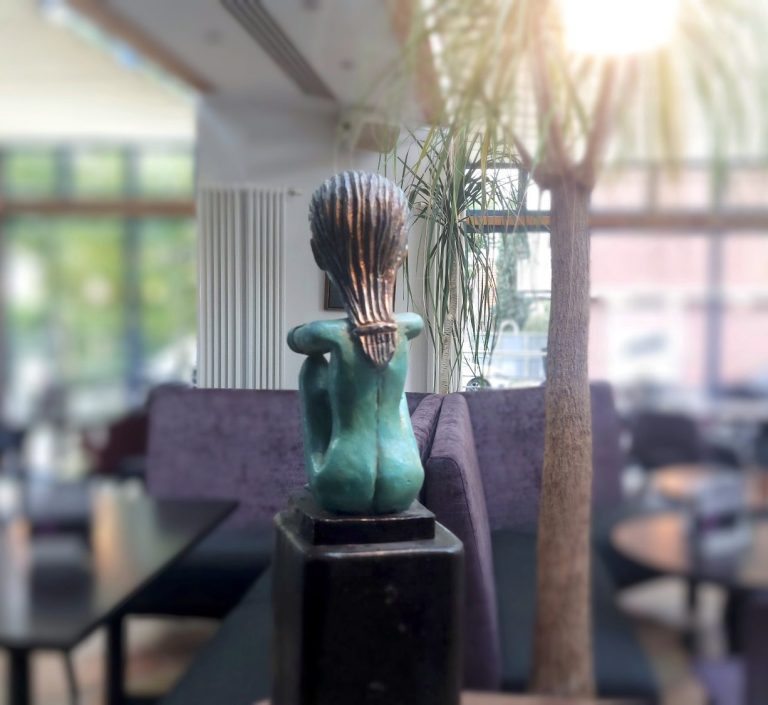 Bronzeskulptur einer Rückenansicht einer Figur in einem modernen Innenraum.