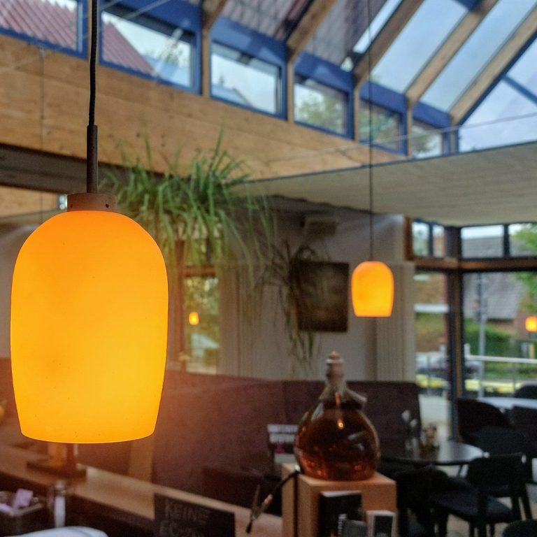 Warme, orangefarbene Pendelleuchten in einem modernen Restaurant mit Fenstern.
