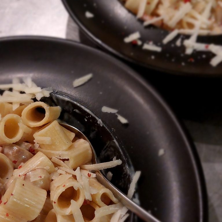 Zwei Teller Pasta mit Käse und roten Pfefferflocken.